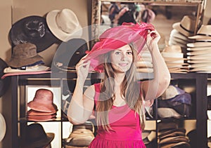 Adult nice woman try on pink boater hat in shopping mall