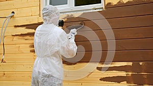 Adult person in respirator and special overall paints wooden wall with paint roller