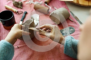 Adult potter master modeling clay cup on table with instruments. Top view, closeup, hands only. Art and business, hobby