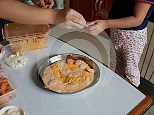 Adult`s hand sending a slice of sausage to a baby`s hand to be placed on a pizza dough