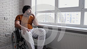 Adult sad man in a wheelchair sitting near the window