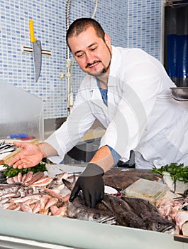 Adult seller shows hands fish on counter photo