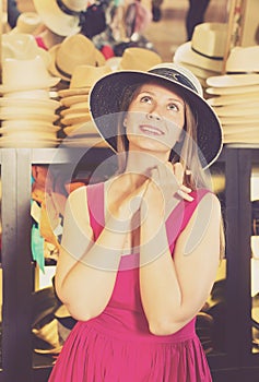 Adult smiling woman try on boater hat in shopping mall