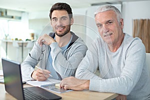 adult son helping senior father with computer at home