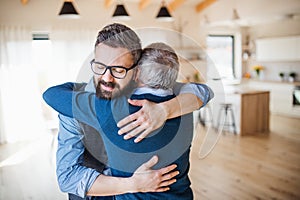 An adult son and senior father indoors at home, hugging.