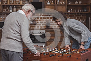 adult son and senior father playing table soccer