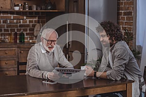 adult son and senior father reading business newspaper