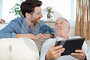 adult son and senior father with tablet sitting on sofa