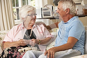 Adult Son Visiting Senior Mother Sitting On Sofa At Home Doing Crochet