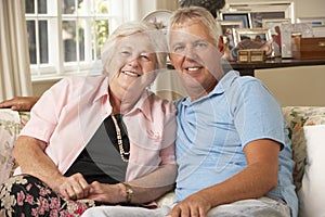 Adult Son Visiting Senior Mother Sitting On Sofa At Home Doing Crochet