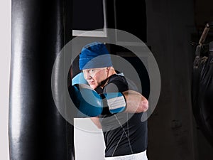 Adult sporty boxer in boxing gloves training with boxing punching bag