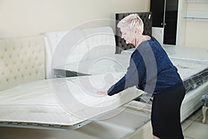 An adult stylish woman with a short-cut blonde chooses a large orthopedic bed with a lifting mattress in a furniture