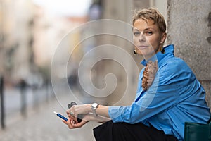 Adult stylish woman with short hair sitting on the european street and holding an electronic cigarette - looking in the