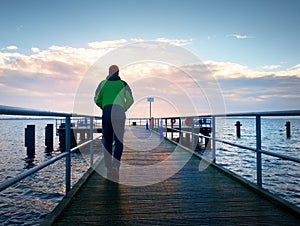 Adult tall man on pier board look over sea to morning Sun. Smooth water level