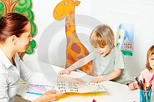 Adult teaches little kids to read letters in the book