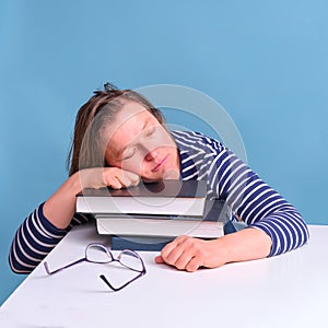 Adult tired woman sleeping on books while studying, blue background