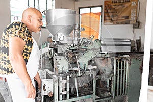 An adult tortilla maker is turning on the nixtamal mill to prepare corn tortillas