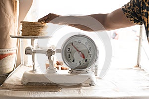 An adult tortilla maker is weighing a kilo of tortillas using an analog scale
