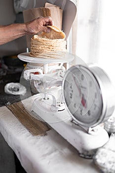 An adult tortilla maker is weighing a stack of tortillas using an analog scale