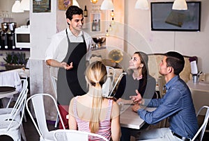 Adult waiter is greeting visitors and taking order.