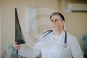 Adult white doctor posing with X-ray at white operation room. Copy space