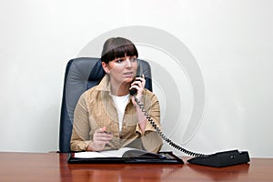 Adult white woman behind a desk in an office talking on