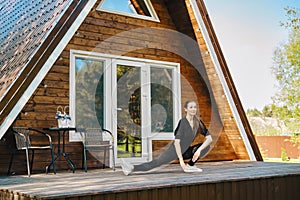 An adult woman in activewear does sports on terrace of log cabin