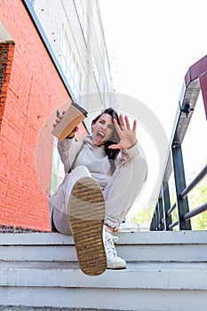 Adult woman in beige suit sits the steps near brick house and holds a reusable thermal mug her hands