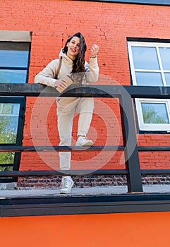 Adult woman in beige suit stands near brick building and holds reusable thermo mug in her hands