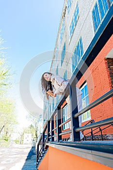 Adult woman in beige suit stands near brick building and holds reusable thermo mug in her hands