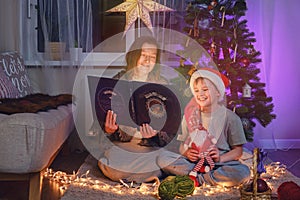 An adult woman and a boy are reading a book by the Christmas tree in