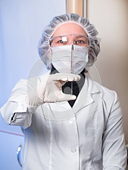 Adult woman closeup protective glasses and medical mask holding in his hand glass syringe