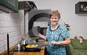 Adult woman cooks stuffed peppers in the kitchen, happy 60 year old woman smiles