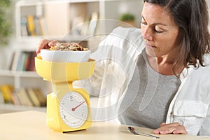Adult woman dieting measuring food with scale at home