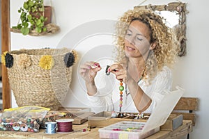 Adult woman doing hand made creations jewelry at home with colorful beads and cords - female people working at home for online