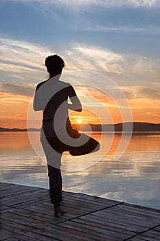 Adult woman doing yoga exercises at sunset