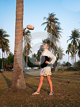 Adult woman in dress standing under a palm tree and catches a coconut