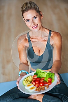 Adult woman eating healthy lunch and sitting on yoga mat