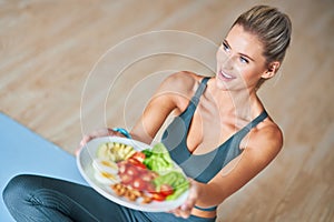 Adult woman eating healthy lunch and sitting on yoga mat