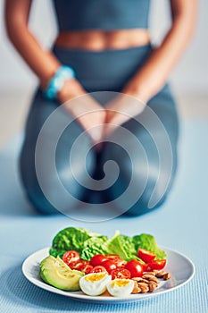 Adult woman eating healthy lunch and sitting on yoga mat