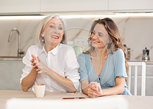 Adult woman and elderly woman drinking tea in kitchen
