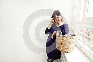 Adult woman emotionally, gesturing, talking on phone . dirty laundry basket with clothes. homework concept