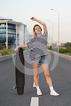 Adult woman enjoy skating on longboard on empty city street. Happy cheerful woman holding skateboard