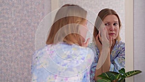 Adult woman examining her face in the mirror. Face treatment concept.