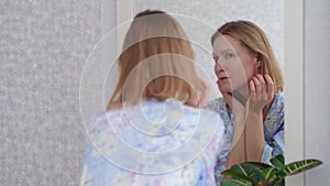 Adult woman examining her face in the mirror reflection.