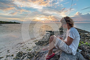 Adult woman with eyeglasses reading ebook relaxing at tropical beach dramatic sky holidays vacation concept