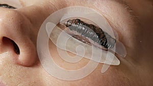Adult woman face on modern eyelash lamination procedure in a professional beauty salon. Master apply black dye paint to