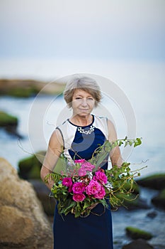 Adult woman florist demonstrates flower bouquet on background of the sea or Ocean and stones summern