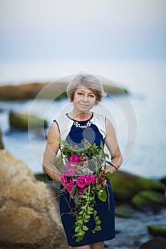 Adult woman florist demonstrates flower bouquet on background of the sea or Ocean and stones summern