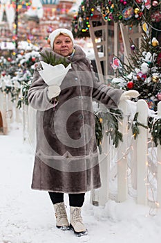 an adult woman in a fur coat on a festive square with a bouquet of Christmas trees.